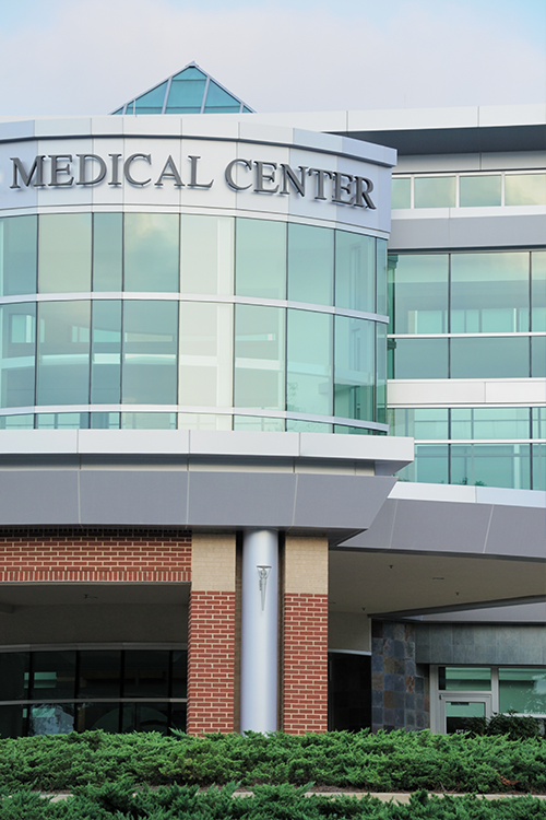 A generic medical center photo of a glass and brick building with an arching triangular shaped top.