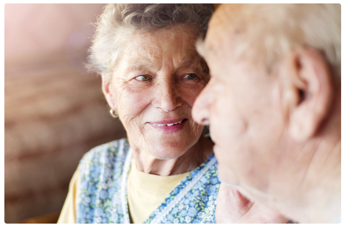 An elderly woman smiles at her husband as they discuss an agitation with dementia clinical research study.