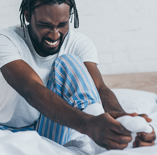 A man holds his foot grimacing in pain from Diabetic Peripheral Neuralgia (DPN).